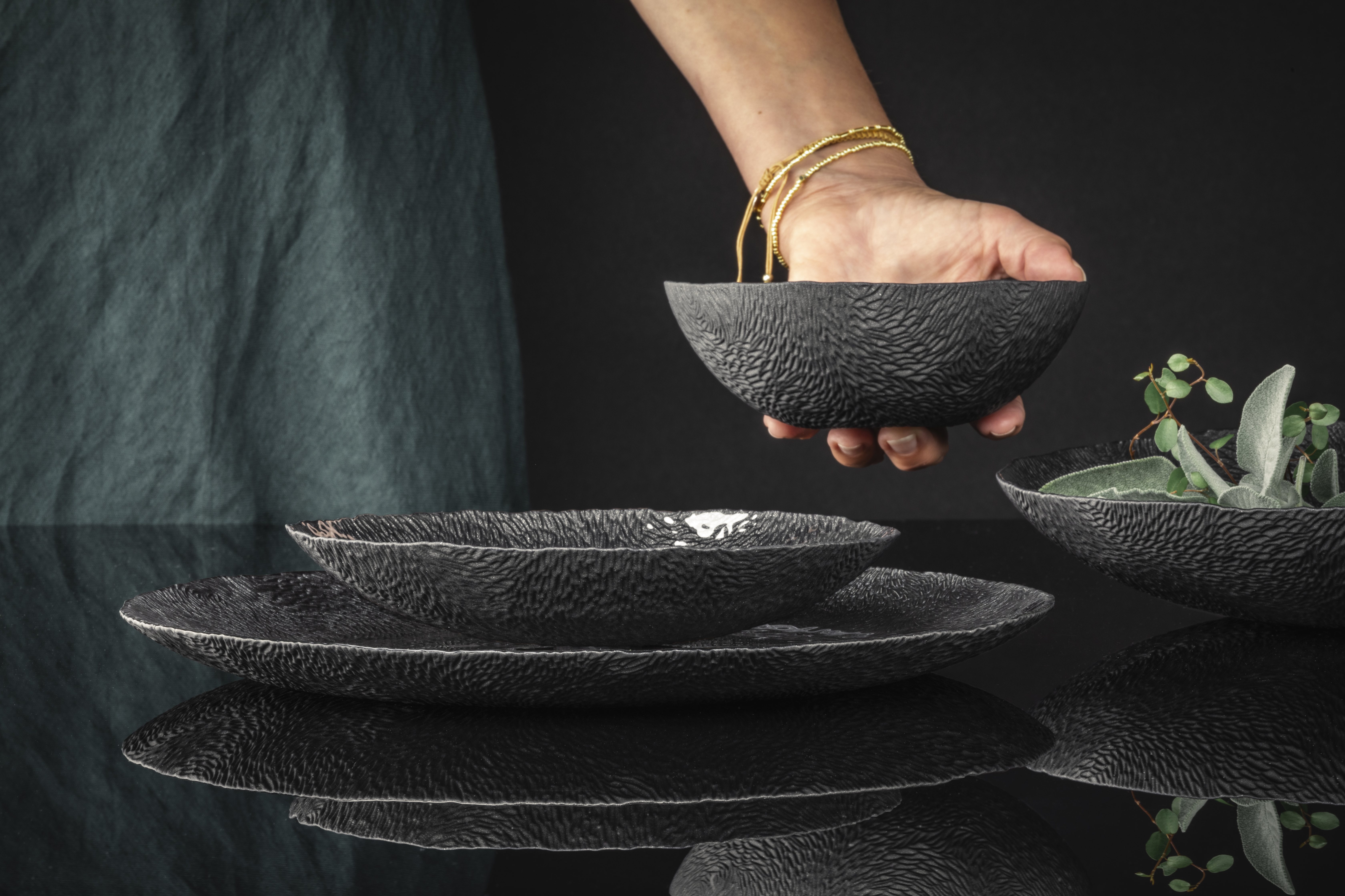 One hand places a black bowl on the table next to the others